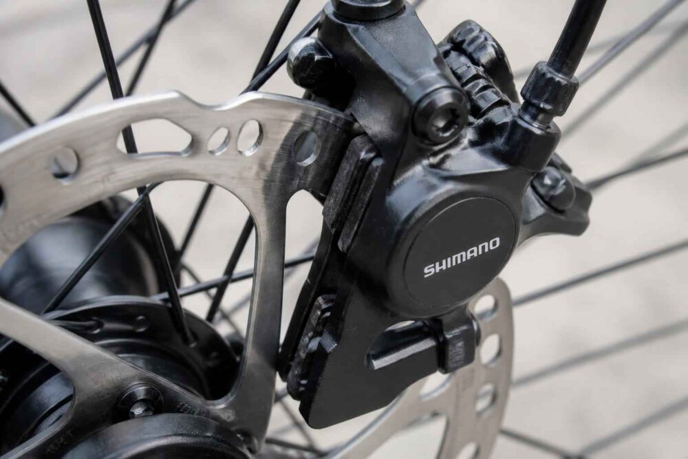 Zbliżenie na czarny zacisk Shimano i srebrną tarczę hamulcową roweru